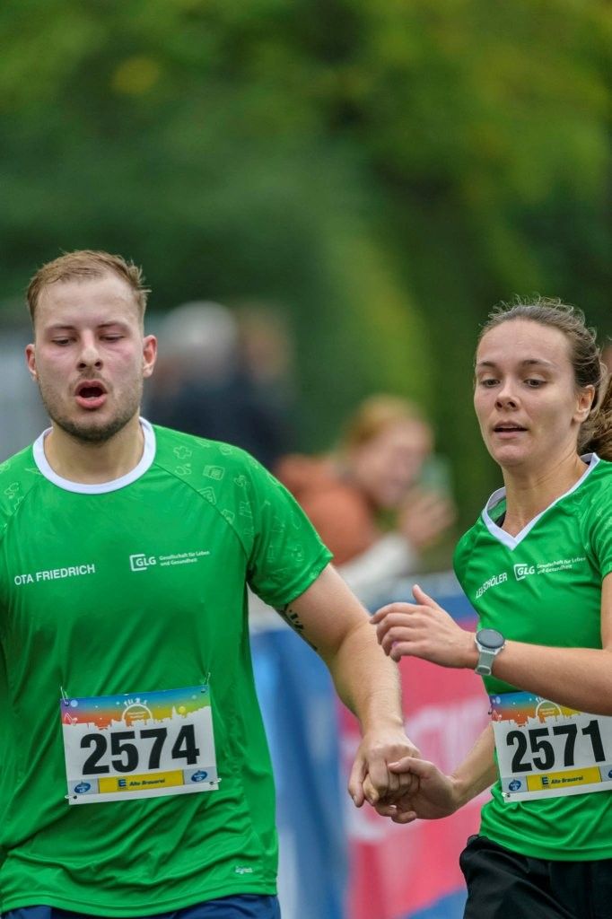 Läufer und Läuferin in grünen Shirts laufen beim 20. Eberswalder Stadtlauf Hand in Hand auf das Ziel zu