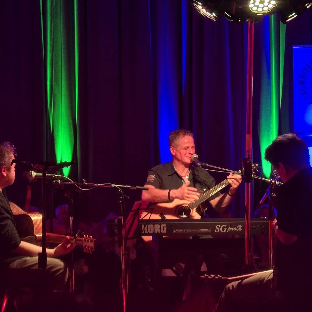 Musiker mit Gitarre im grünen Bühnenlicht beim Songwriter-Circle 2025